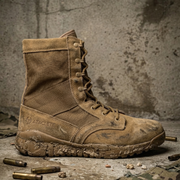 Brown military boot with visible brand logo on a textured surface with ammunition and fabric.