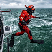 A diver in a red and black dry suit with a helmet and flippers jumps from the side of a helicopter over choppy green-gray ocean water under an overcast sky.